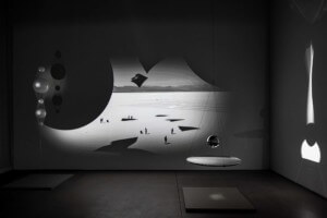 black and white photo with screen projection and swinging ball sculpture