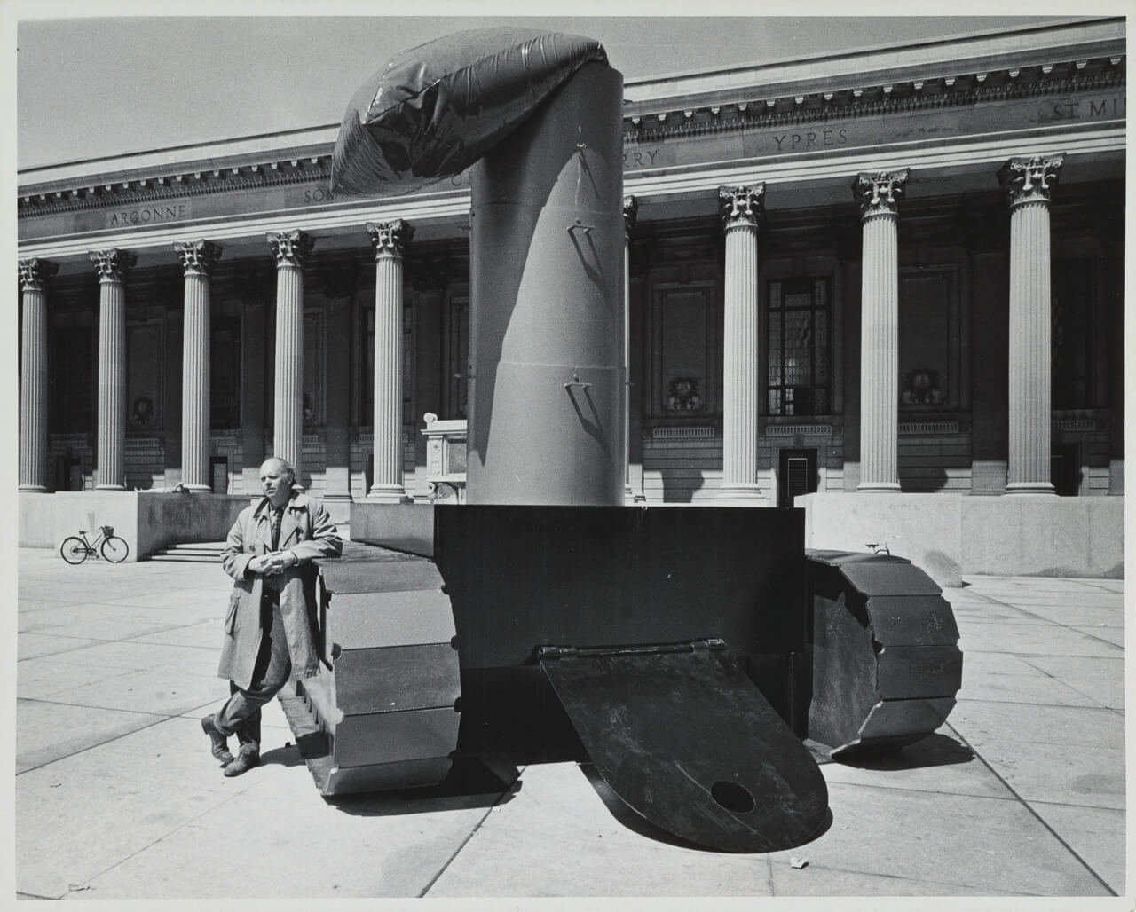 claes oldenburg leaning on a lipstick sculpture in a plaza
