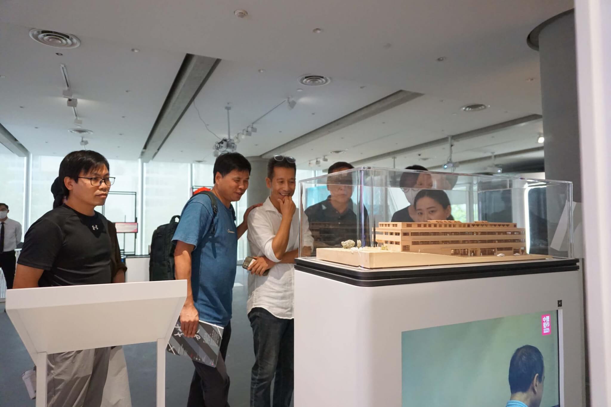 people looking at wooden model in glass display case