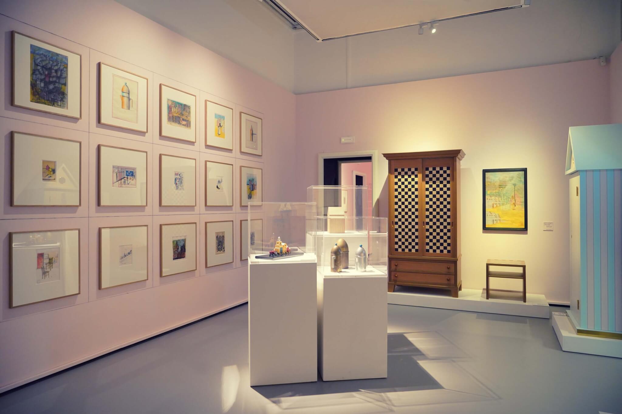 exhibition room with pink walls and sketches and objects on display