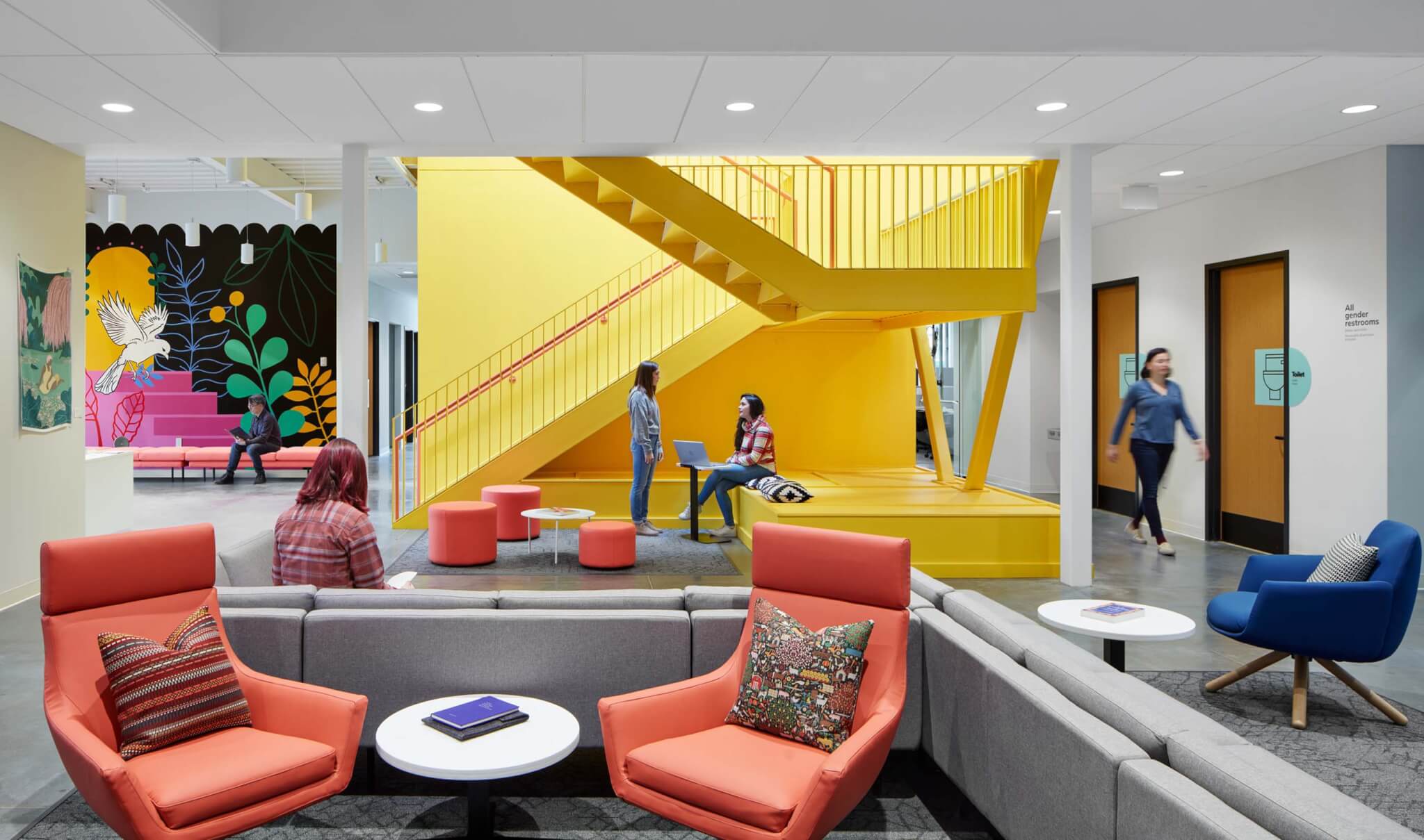lounge space with orange chairs and bright yellow staircase in the background