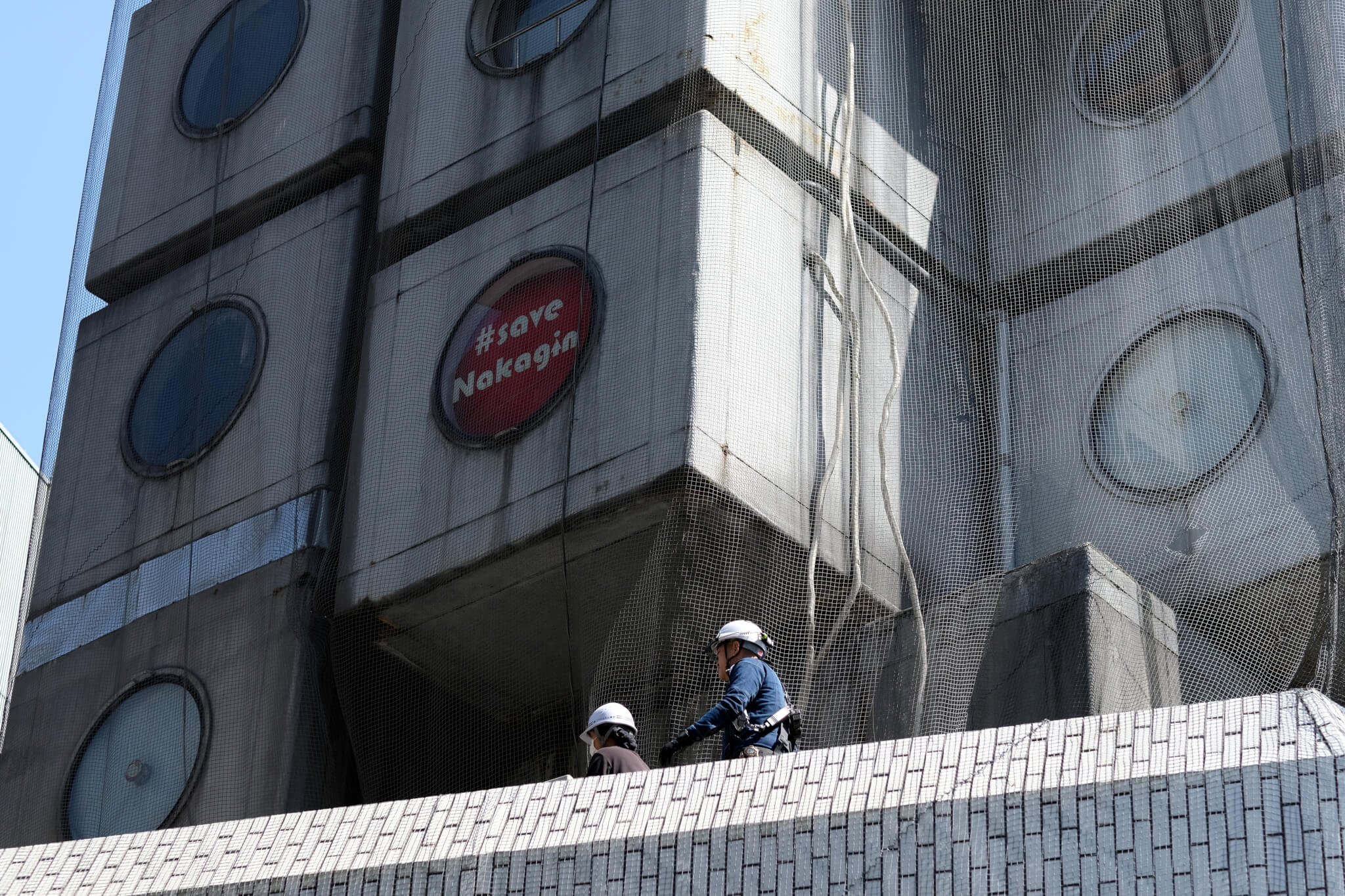 construction workers on tower with save nakagin sign