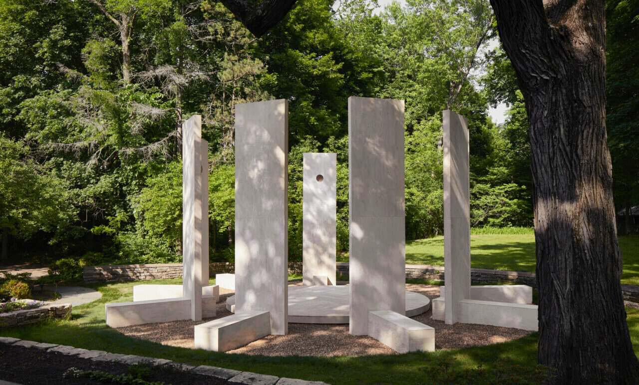 Installation surrounded by trees of tall chair like structures in a circle.