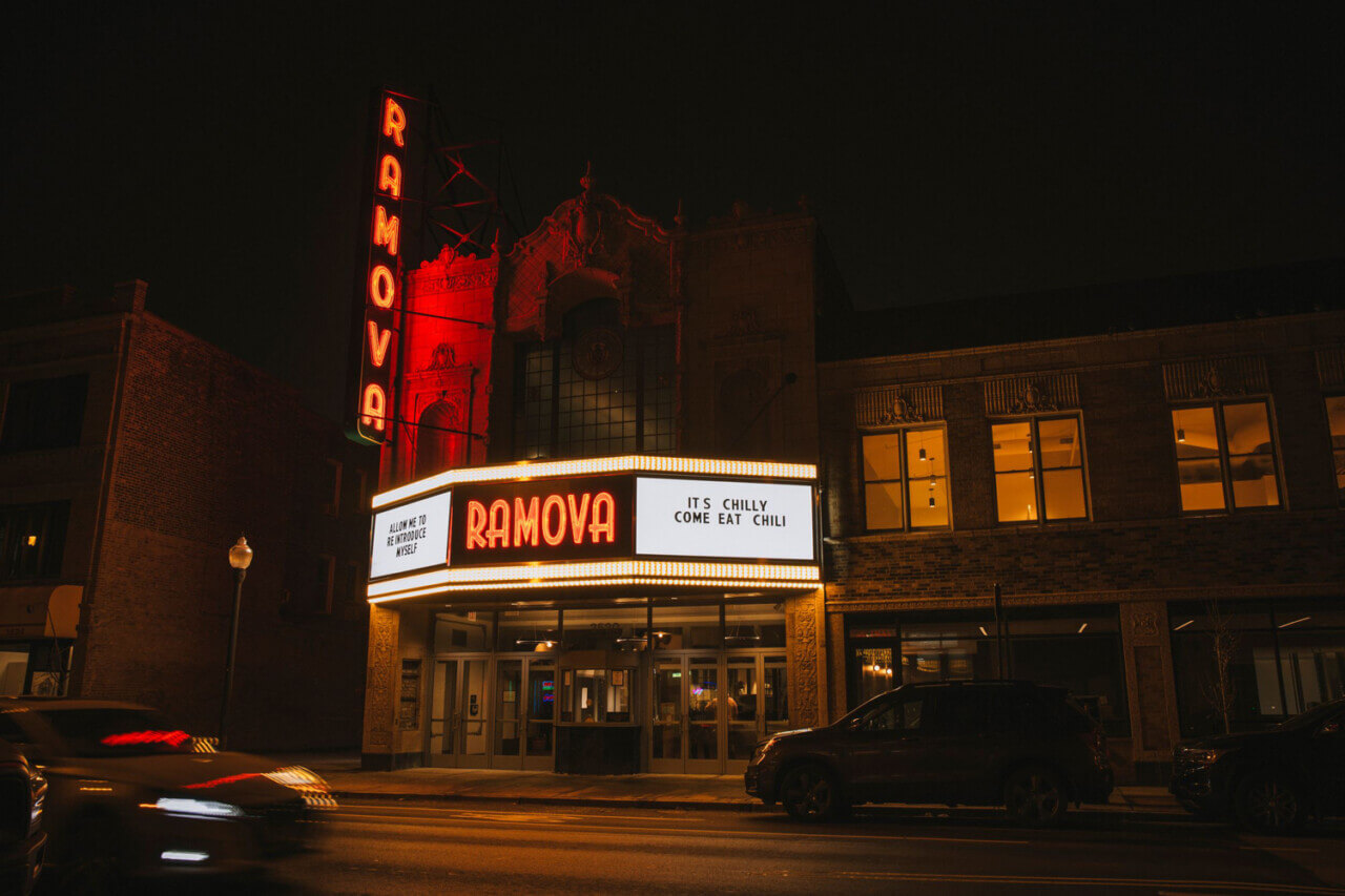 Exterior of a theatre at night with a neon red marquee, with a title reading "allow me to introduce myself."