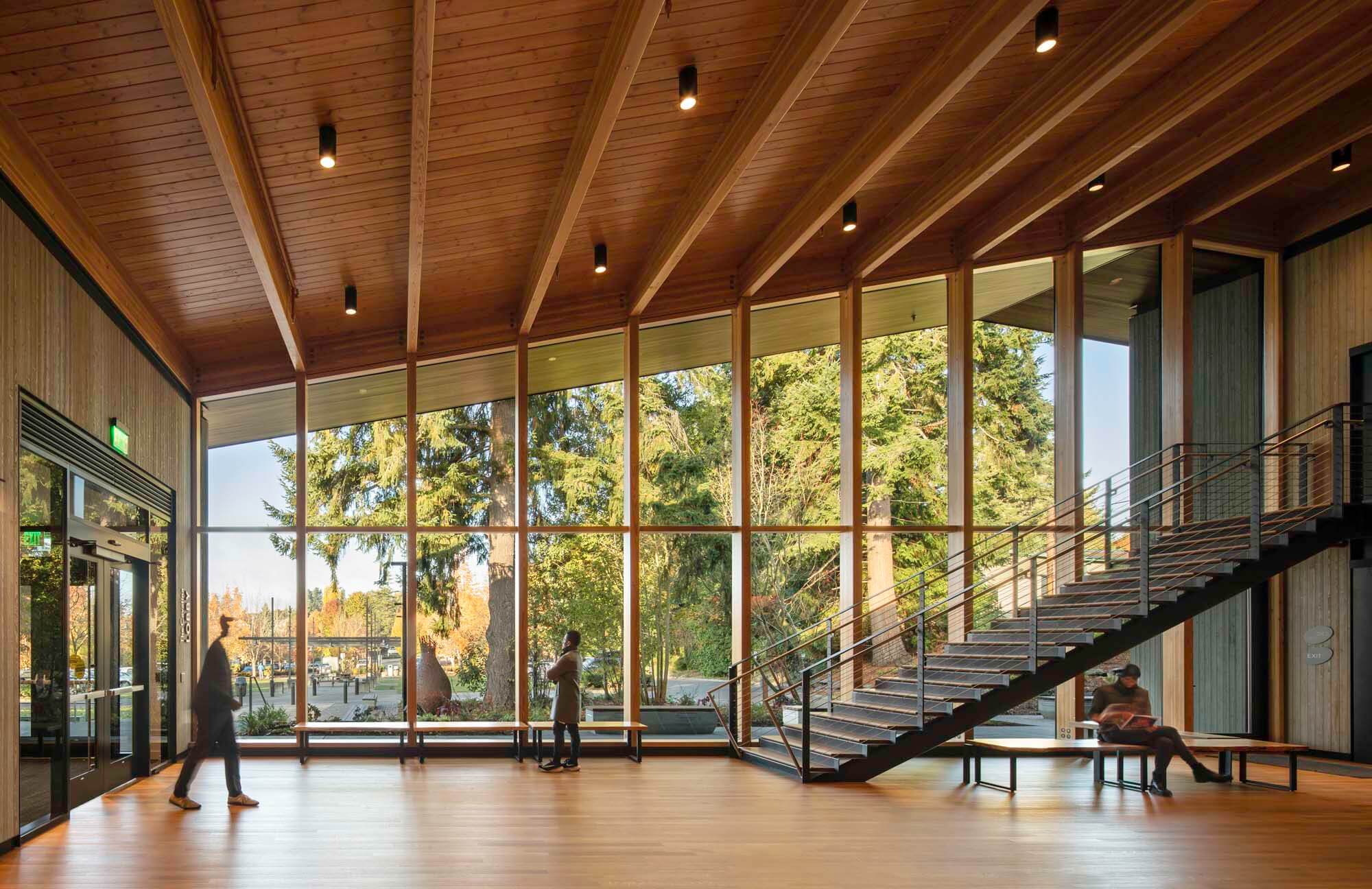 A lobby with wood and blackened steel fixtures, with a background of woodland landscape peeking from the glass curtain wall.