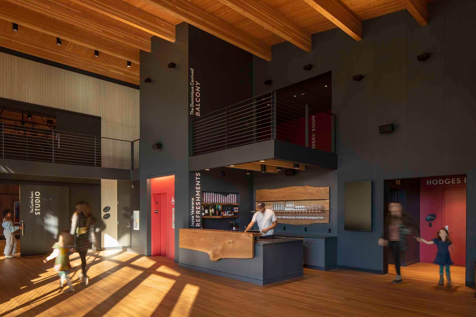 Lobby with a wooden roof and a black wall. A steel balcony and a bar area.