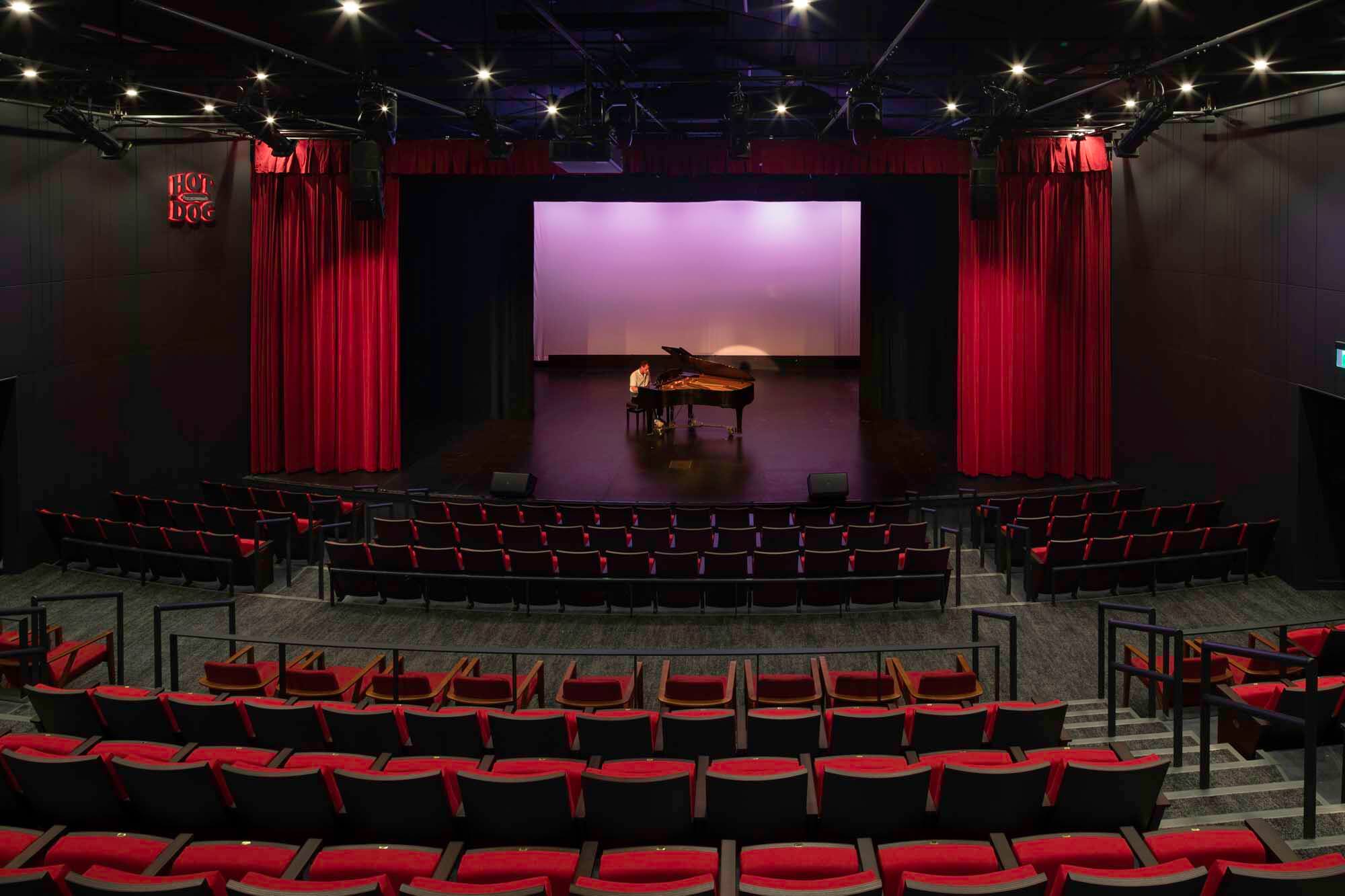 An auditorium with red seats and a piano onstage. 