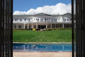 Image of a grand white estate, with a green lawn and a pool.